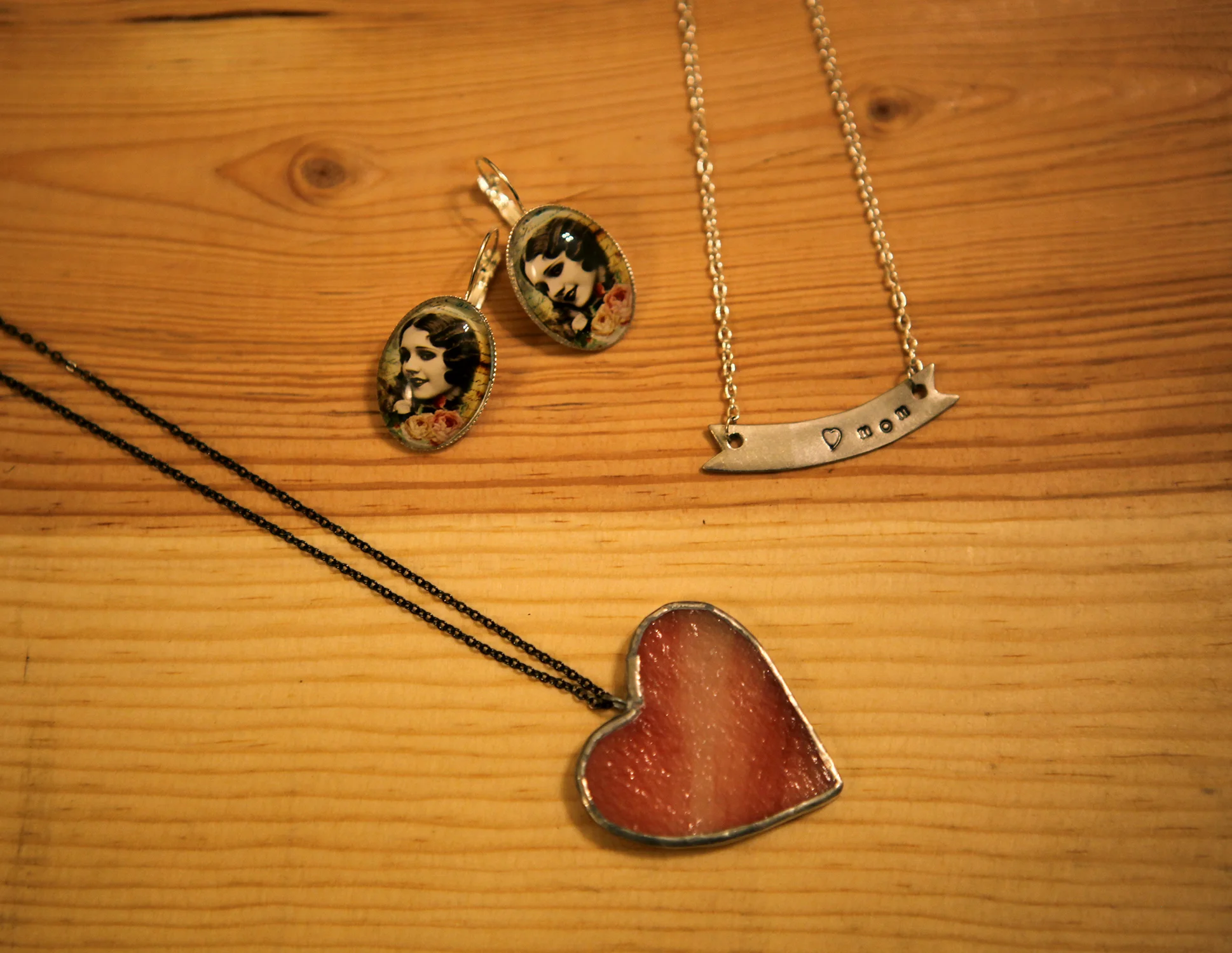 Glass heart necklace made by Glass Action, $25.00. Silver "mom" banner necklace by Dear Darlington, $24.00. Lady oval earrings by Trollaphant, $15.00.