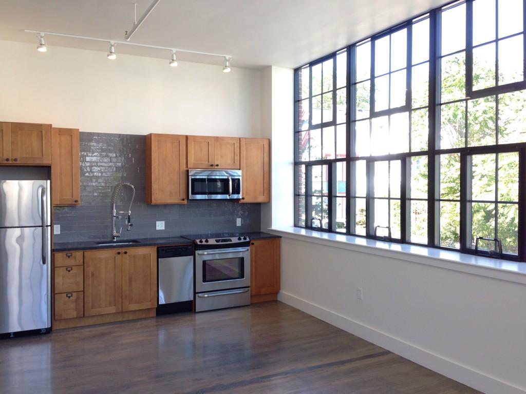 A second story loft space with original hardwood floors, full size windows, tall ceilings, and stainless appliances.