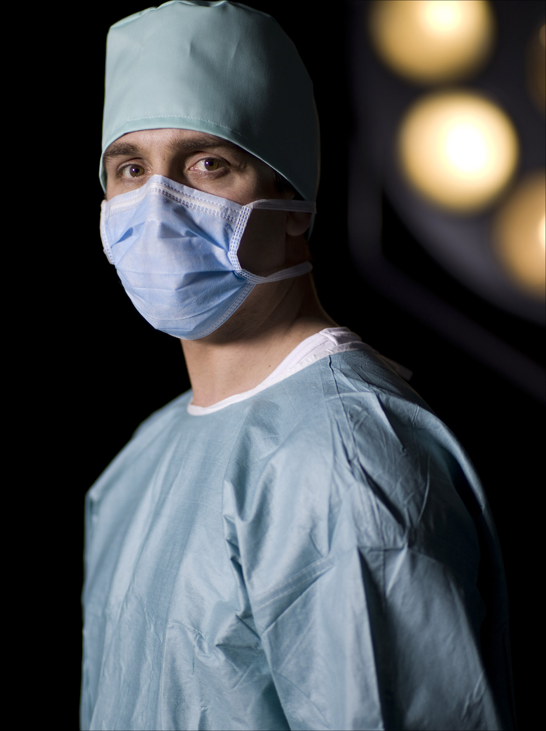 Portrait of a surgeon in mask and gown with operating light in the background