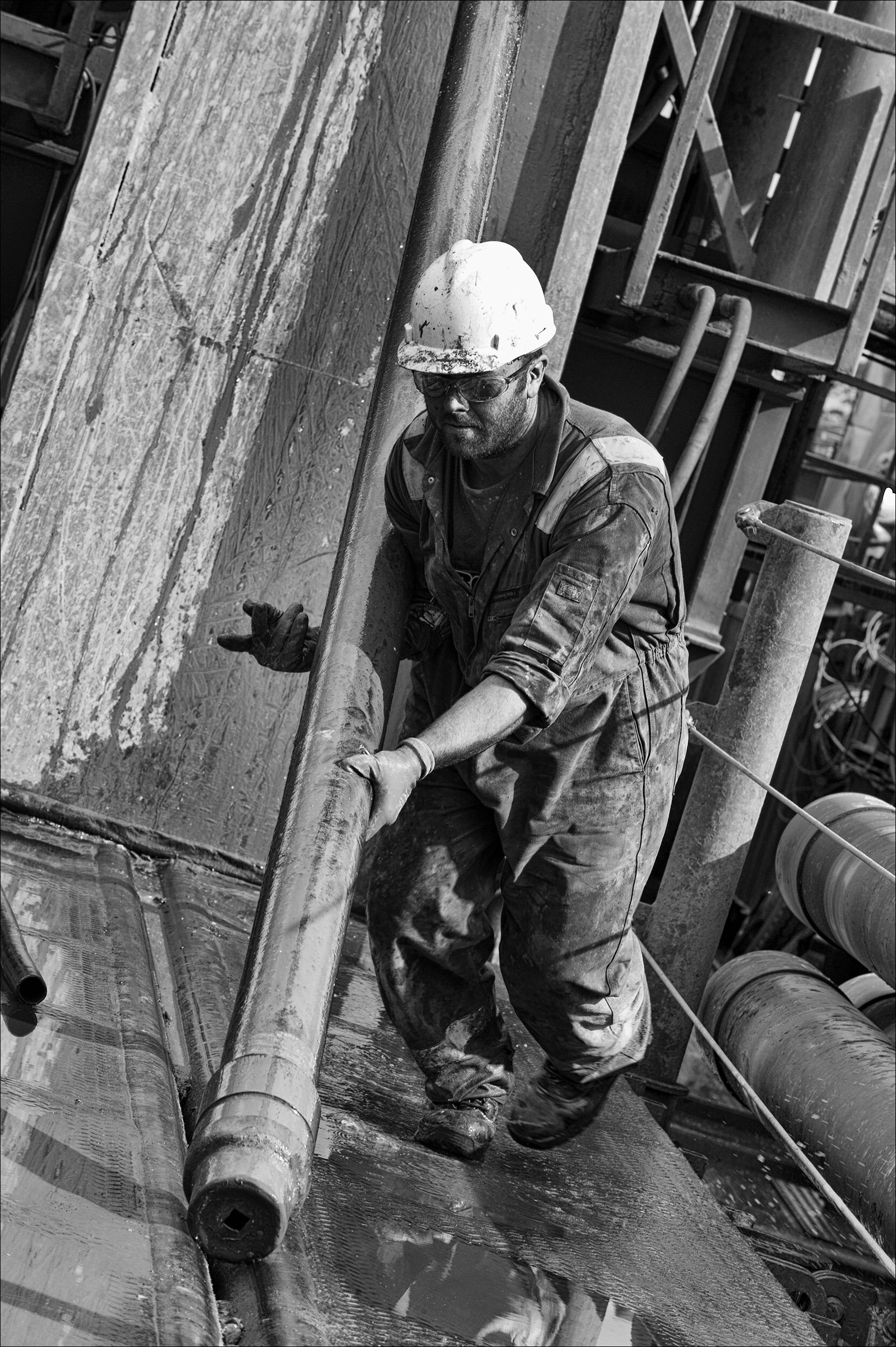 man in PPE moving a heavy pipe on drilling rig