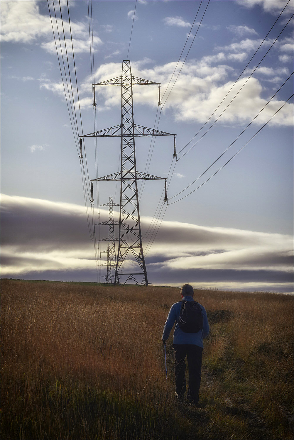 Hiker walking through fields underneath an electricity pylon