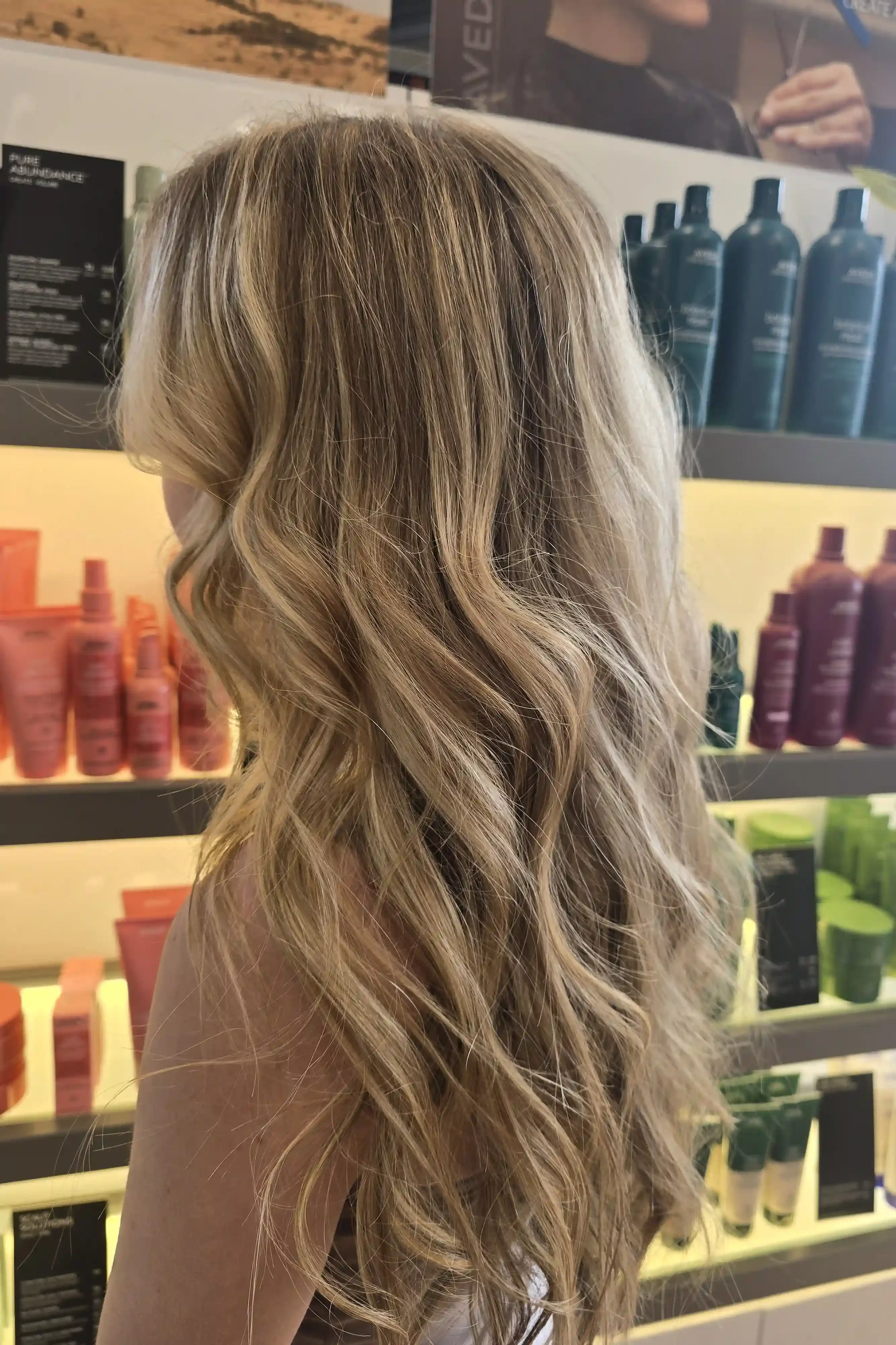 Long dimensional blonde balayage featuring a soft root melt, bright face-framing highlights, and seamless ribbons of blonde for a natural, lived-in finish. Styled with loose waves to showcase depth, brightness, and movement while providing a low-main