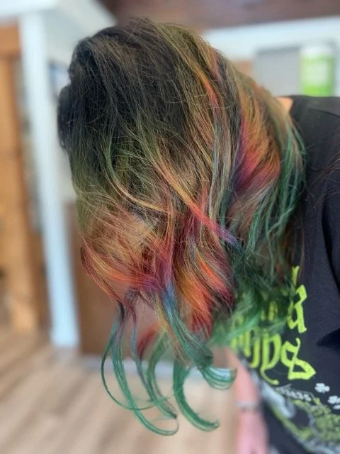 Vibrant rainbow hair color with green, red, and orange highlights styled at Chroma Salon Seattle. Expert stylists create bold, creative hair color transformations for unique, personalized looks.