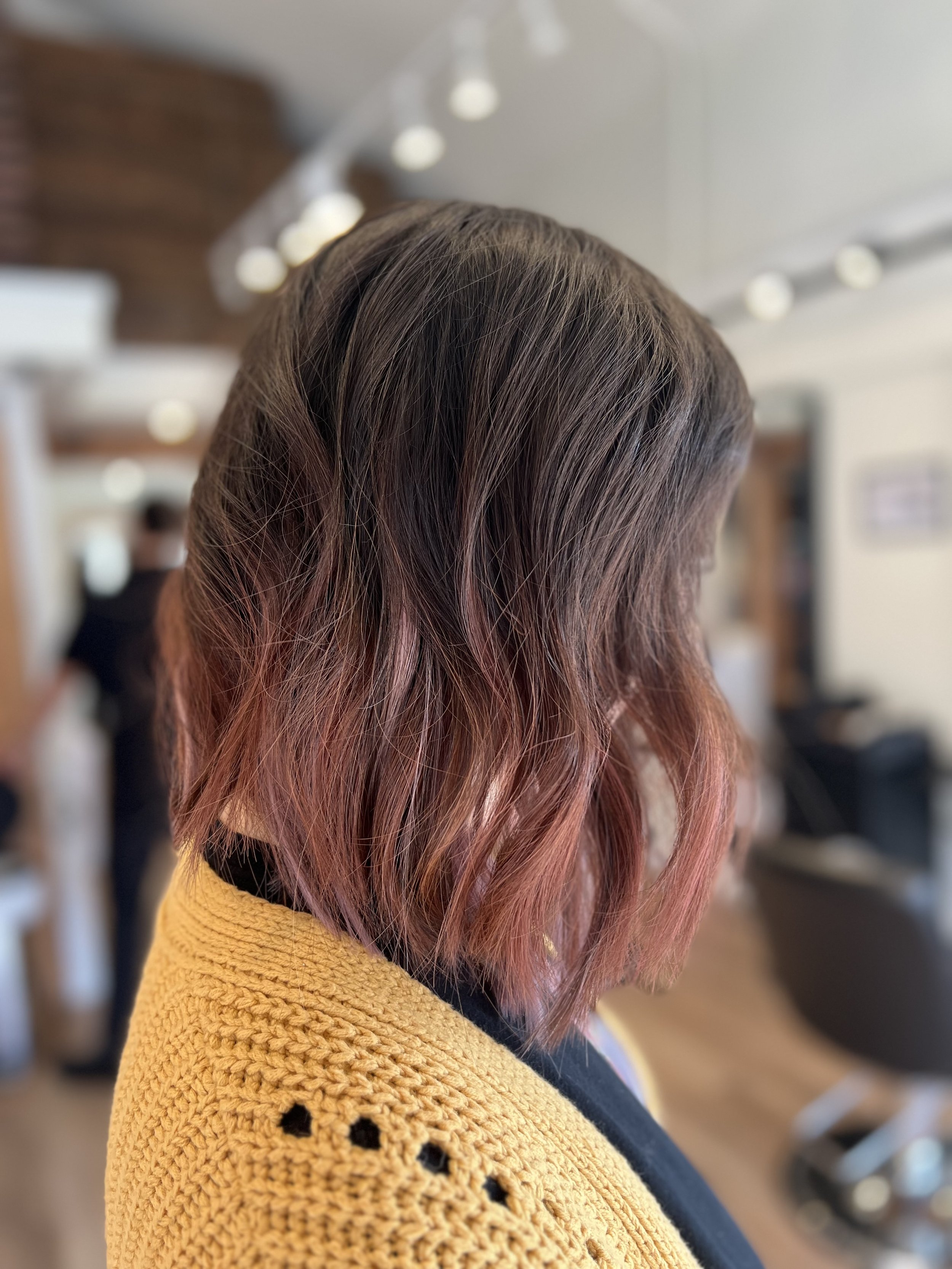 Woman with wavy shoulder-length brown hair, wearing a yellow crochet shawl, in a salon setting.