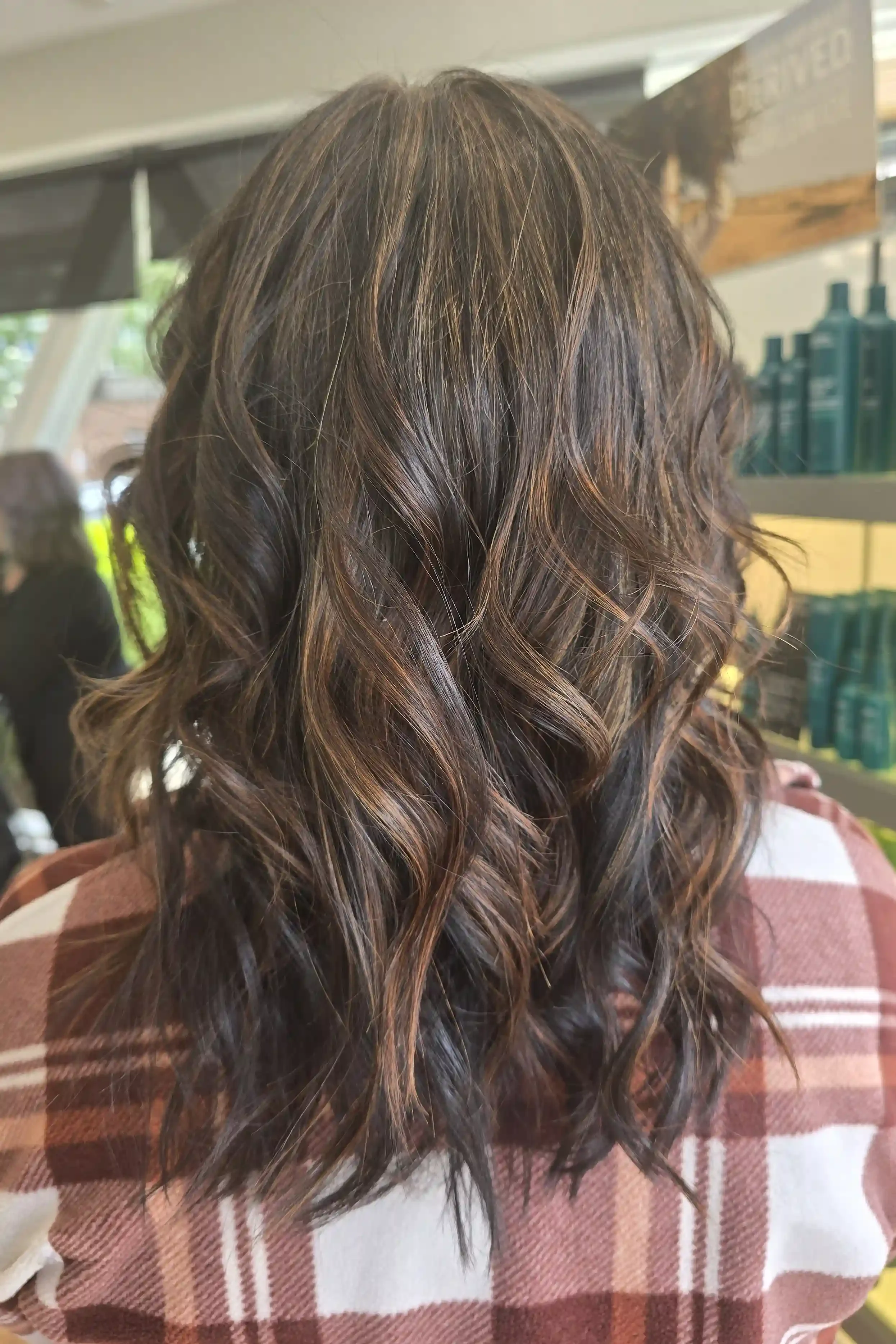 Rich brunette balayage with soft copper and caramel ribbons woven through a deep chocolate base, styled in loose, tousled waves. The dimensional color adds warmth, shine, and movement while maintaining a natural, low-maintenance finish. Hair color an