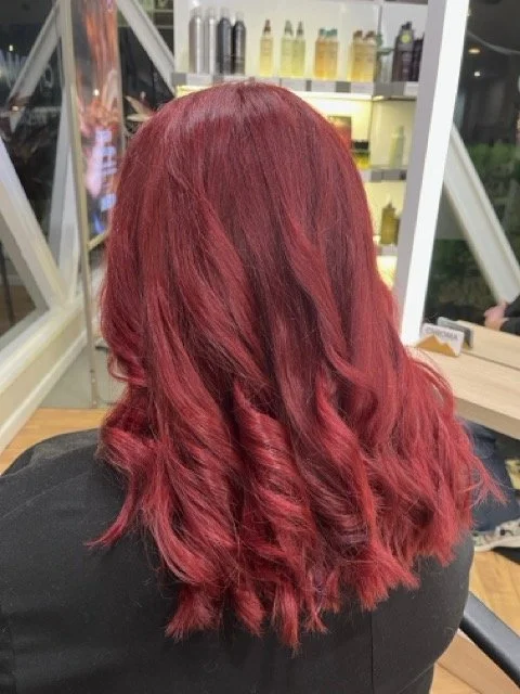 Vibrant red Aveda hair color with soft curls and rich dimension, created at Chroma Salon Seattle by expert hair color specialists.