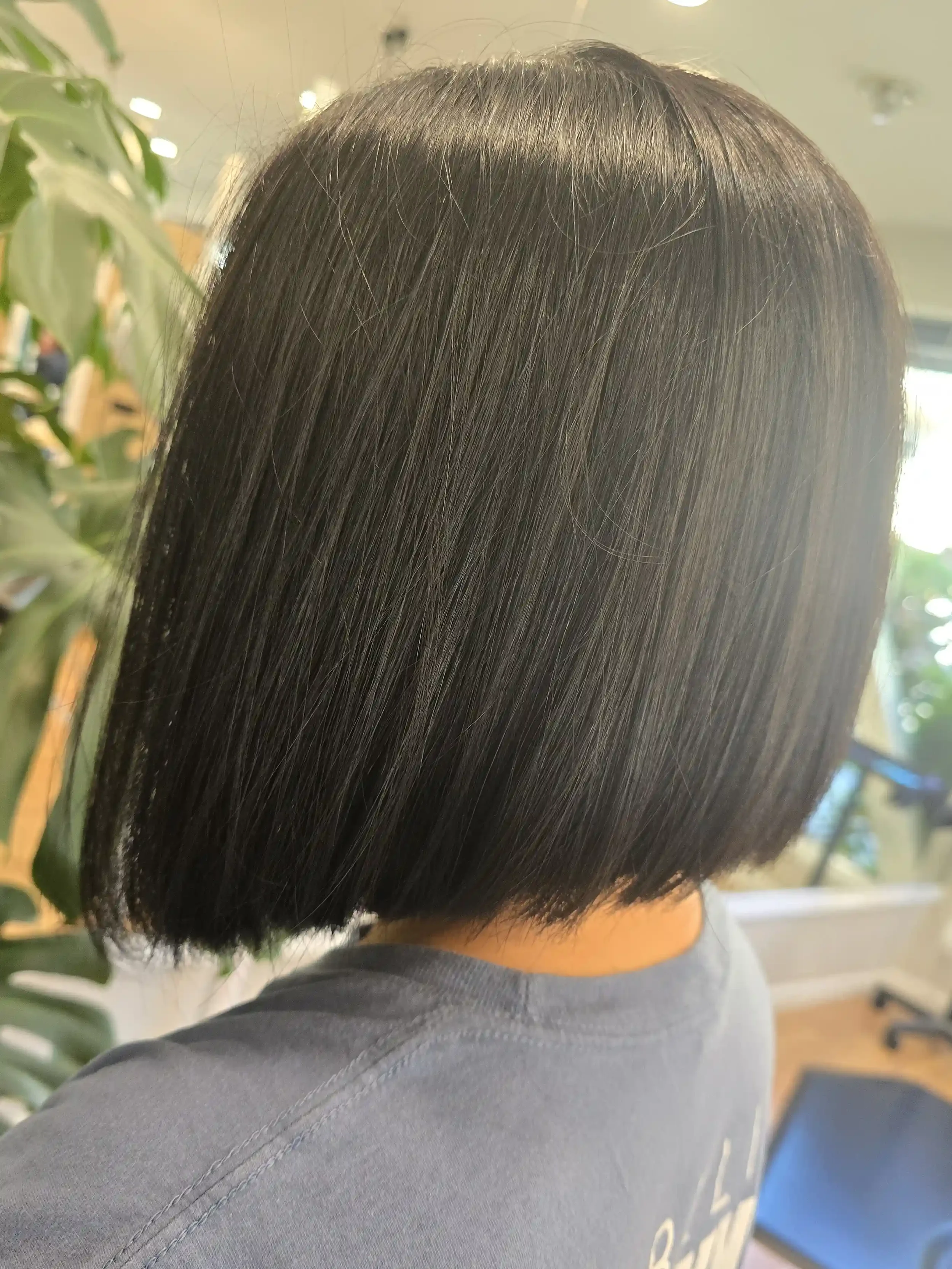 Sleek black bob haircut featuring a precision one-length shape, glossy shine, and clean perimeter. This polished, chin-length style enhances hair density and creates a modern, sophisticated finish with smooth movement and exceptional light reflection
