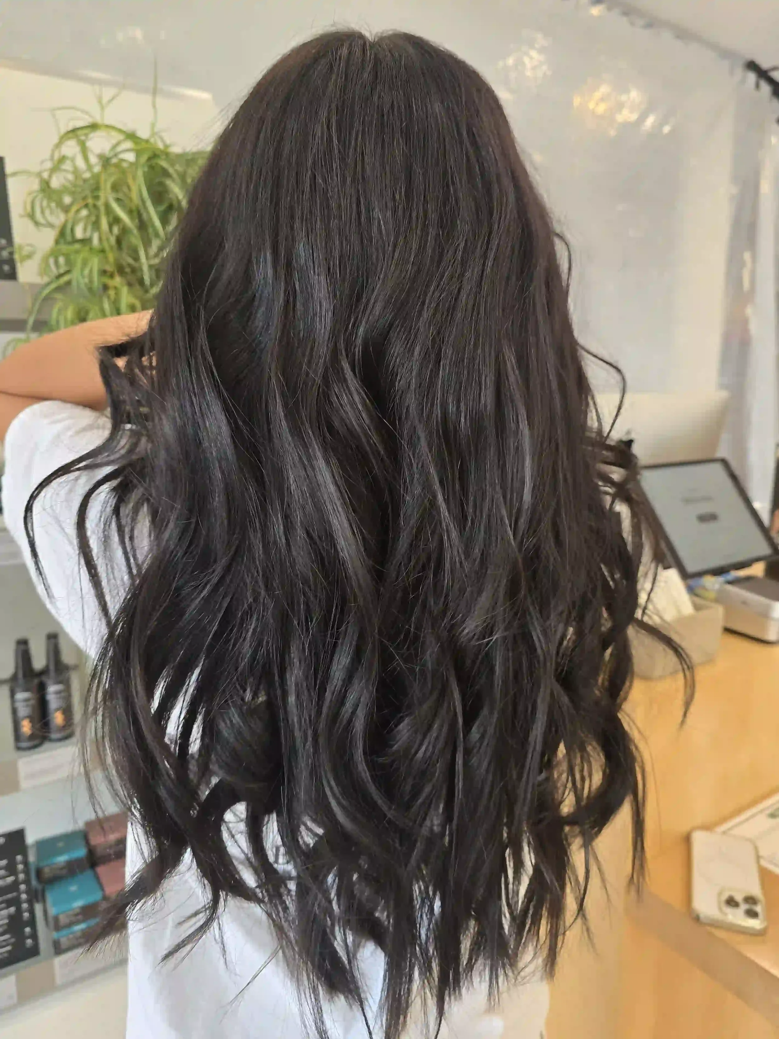 Rich, dark chocolate brunette hair with subtle natural-looking dimension and a deep, glossy finish. Long, flowing layers are styled in loose, tousled waves that create beautiful movement, volume, and texture. Hair by Jhana at Chroma Salon Edmonds.