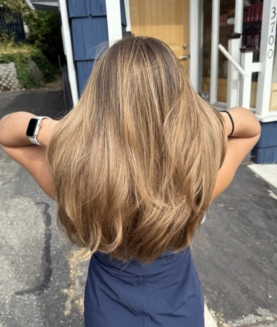 Warm caramel blonde balayage with long, layered haircut and natural dimension, styled at Chroma Salon Seattle for a soft, sunlit finish.