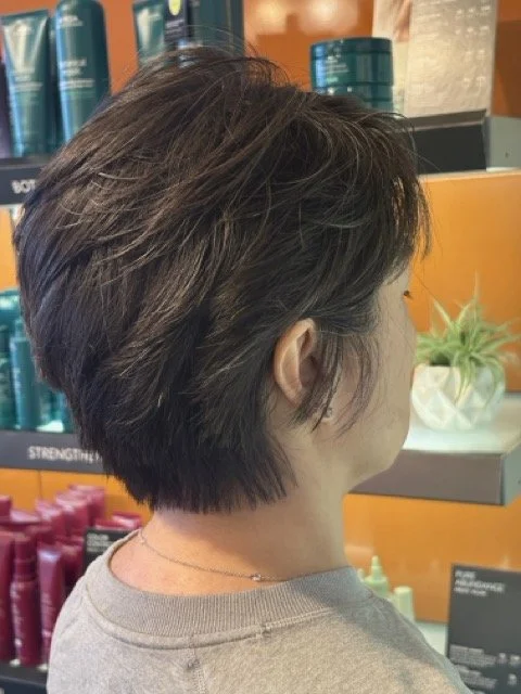 Short textured brunette pixie haircut with soft layers and natural volume, styled at Chroma Salon Lynnwood using Aveda products.