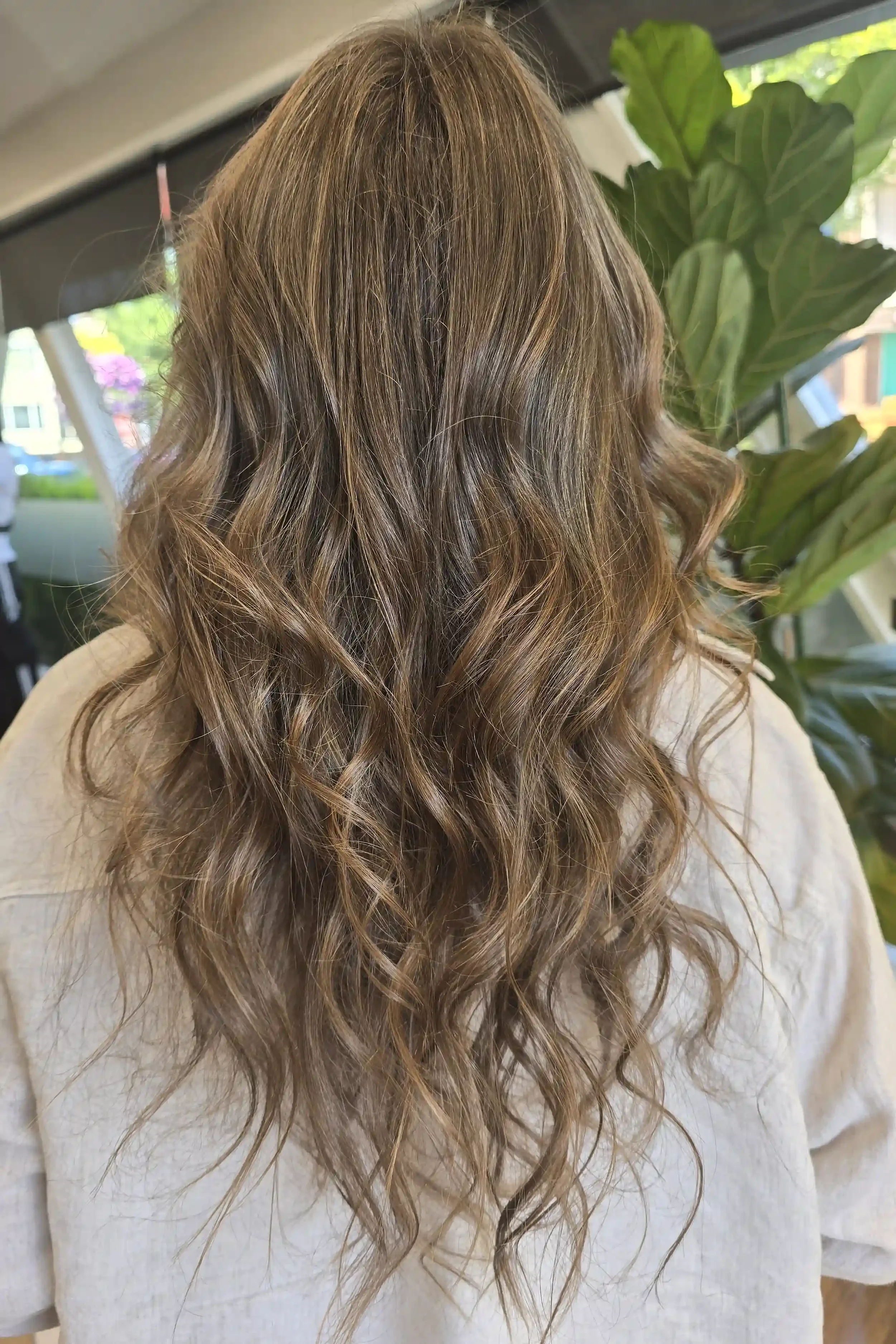 Long lived-in bronde balayage with soft beige-blonde ribbons blended into a medium brunette base for seamless dimension and natural grow-out. Finished with loose beach waves that highlight the multi-tonal color and create effortless movement and shin