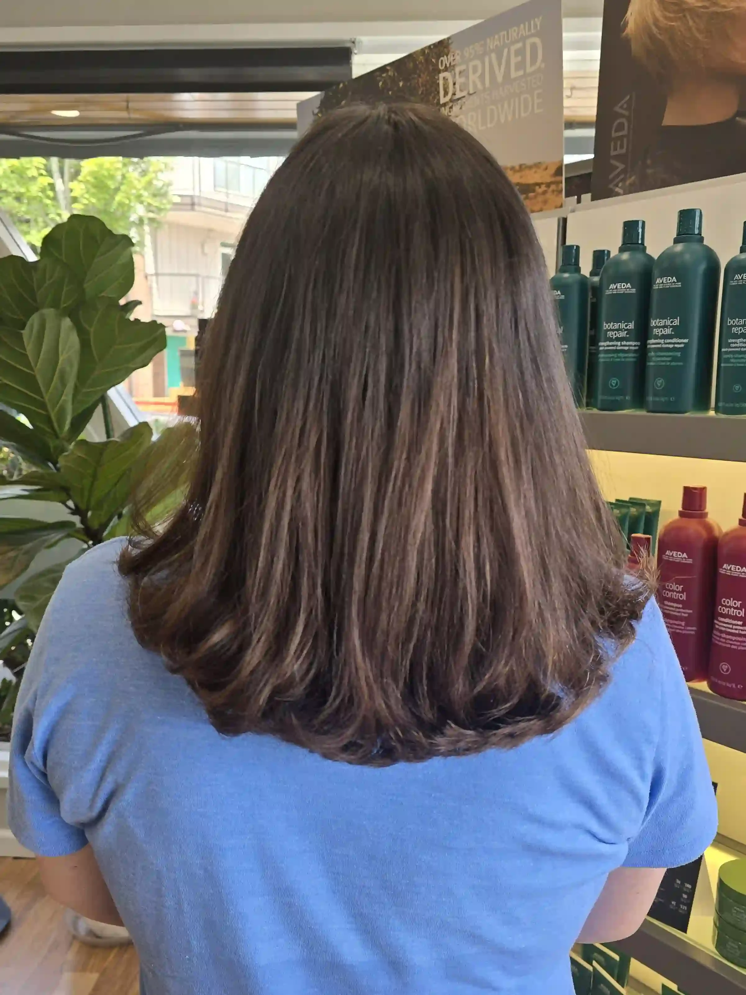 Medium-length brunette hair with long layers, soft face-framing, and a smooth, polished blowout. This timeless haircut adds natural movement, body, and shine while maintaining healthy-looking length and a classic finish. Haircut and styling by Jhana 