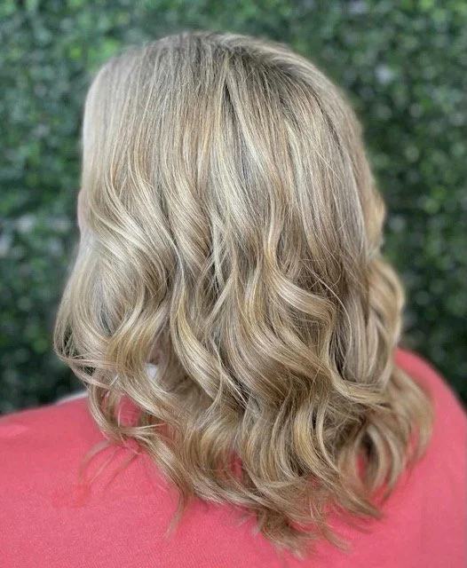 Back view of shoulder-length wavy blonde hair with soft, natural-looking highlights. Styled in loose curls by a Chroma Salon stylist in Seattle.