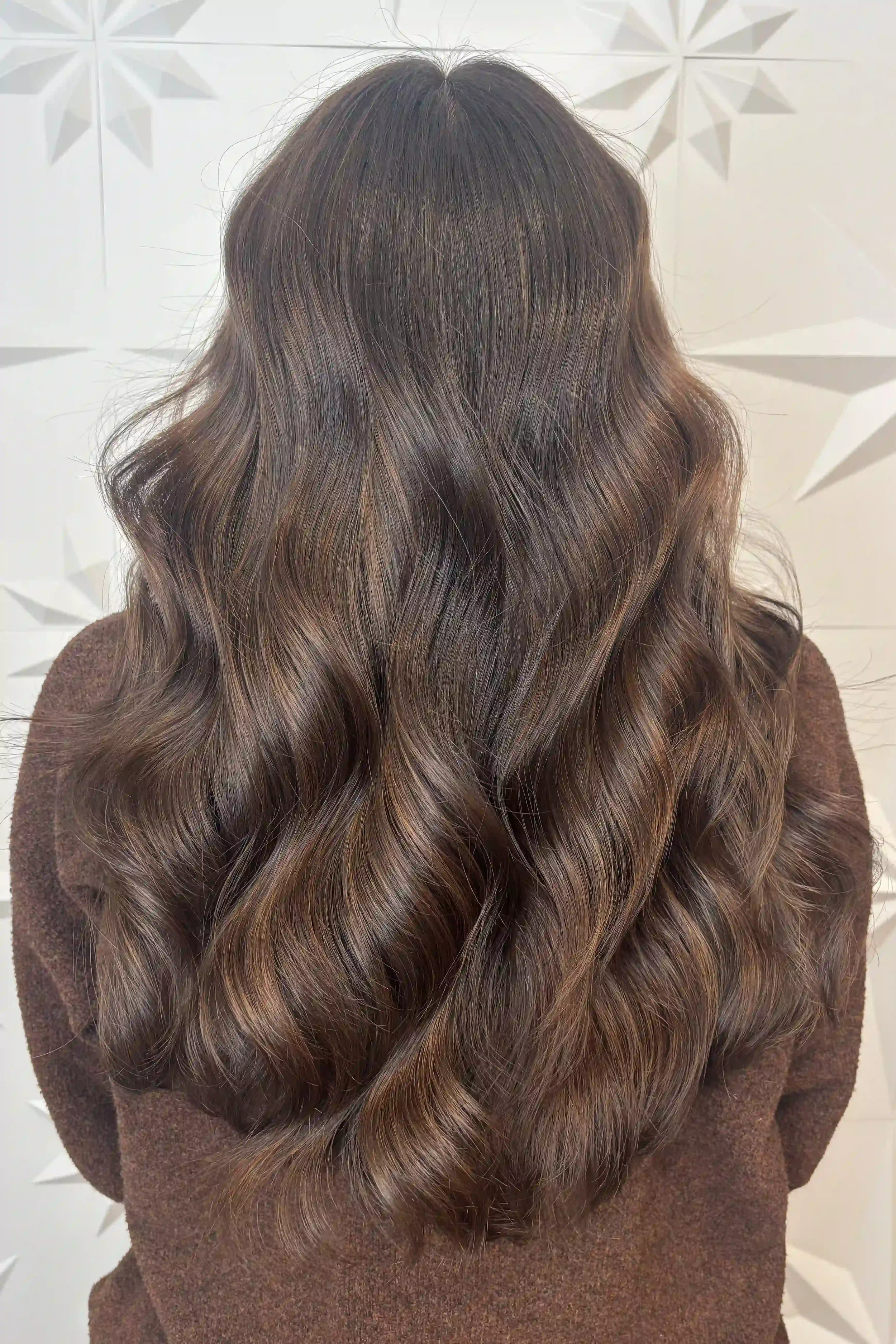 Rich chocolate brunette hair with subtle caramel-brown dimension, styled in soft, flowing waves. Long layers create beautiful movement and fullness, while warm tones add depth and shine. Hair by Alpin at Chroma Salon Queen Anne.