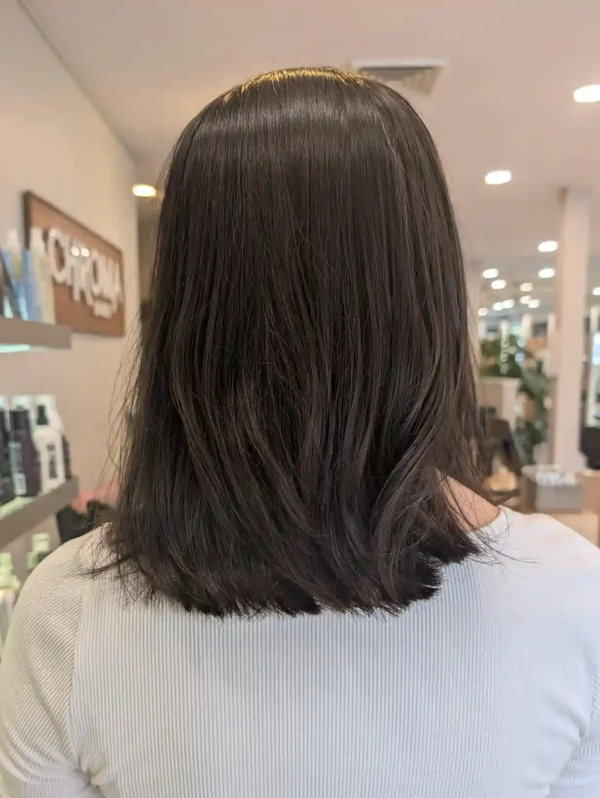 Soft black brunette lob with subtle dimensional shine and clean blunt shaping. Lightweight texture and gentle movement keep the shoulder-length cut polished, modern, and effortlessly wearable.
