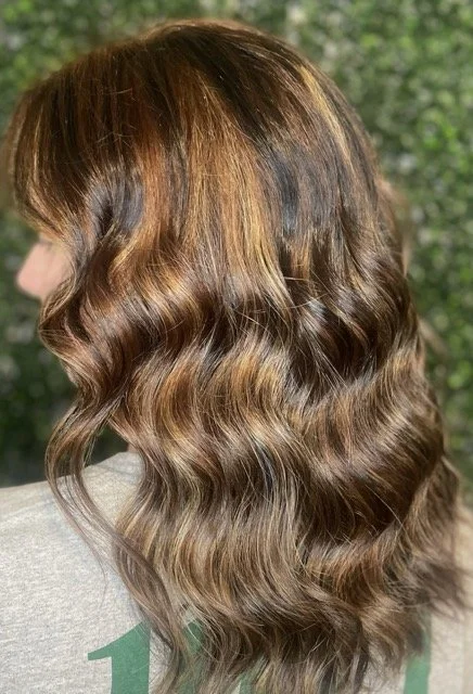 Rich brunette hair with golden caramel highlights and soft waves, created at Chroma Salon Seattle using Aveda color for radiant dimension and shine.