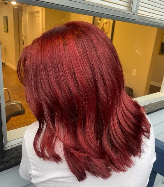 Vibrant red Aveda hair color with soft layered cut, styled at Chroma Salon Seattle. Professional stylists create rich, multidimensional tones for healthy, glossy hair.