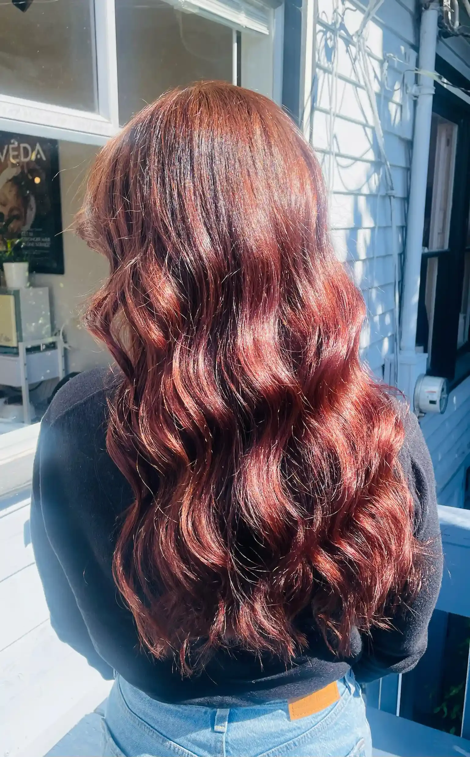 Rich copper mahogany hair color with deep red undertones and luminous shine. This dimensional brunette-to-red transformation features a seamless all-over color application, reflective finish, and soft polished waves that enhance depth, movement, and 