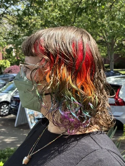 Rainbow vivid hair color with red, orange, yellow, green, blue, and purple tones on a curly shag mullet haircut, styled by Peter at Chroma Salon Queen Anne Seattle.
