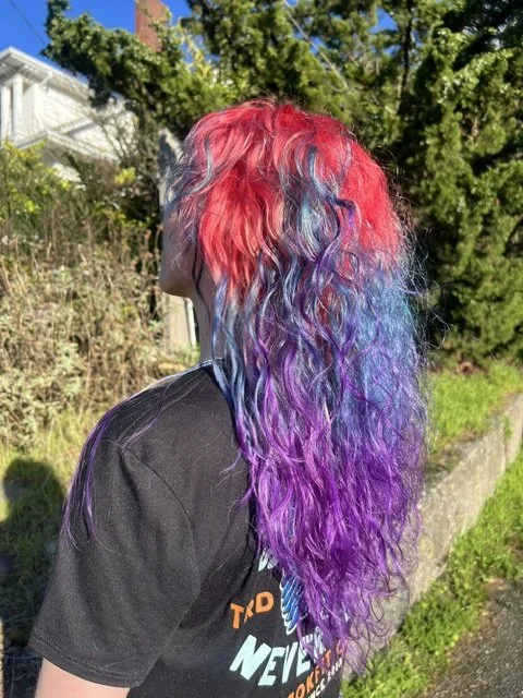 Vivid rainbow hair color with red, blue, and purple tones on long textured hair, created at Chroma Salon Seattle by expert vivid color specialists.
