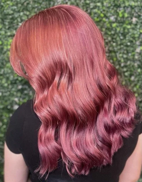 Back view of long, wavy rose gold and magenta hair with a soft shine. Vibrant fashion color styled at a Seattle hair salon using Aveda color products.
