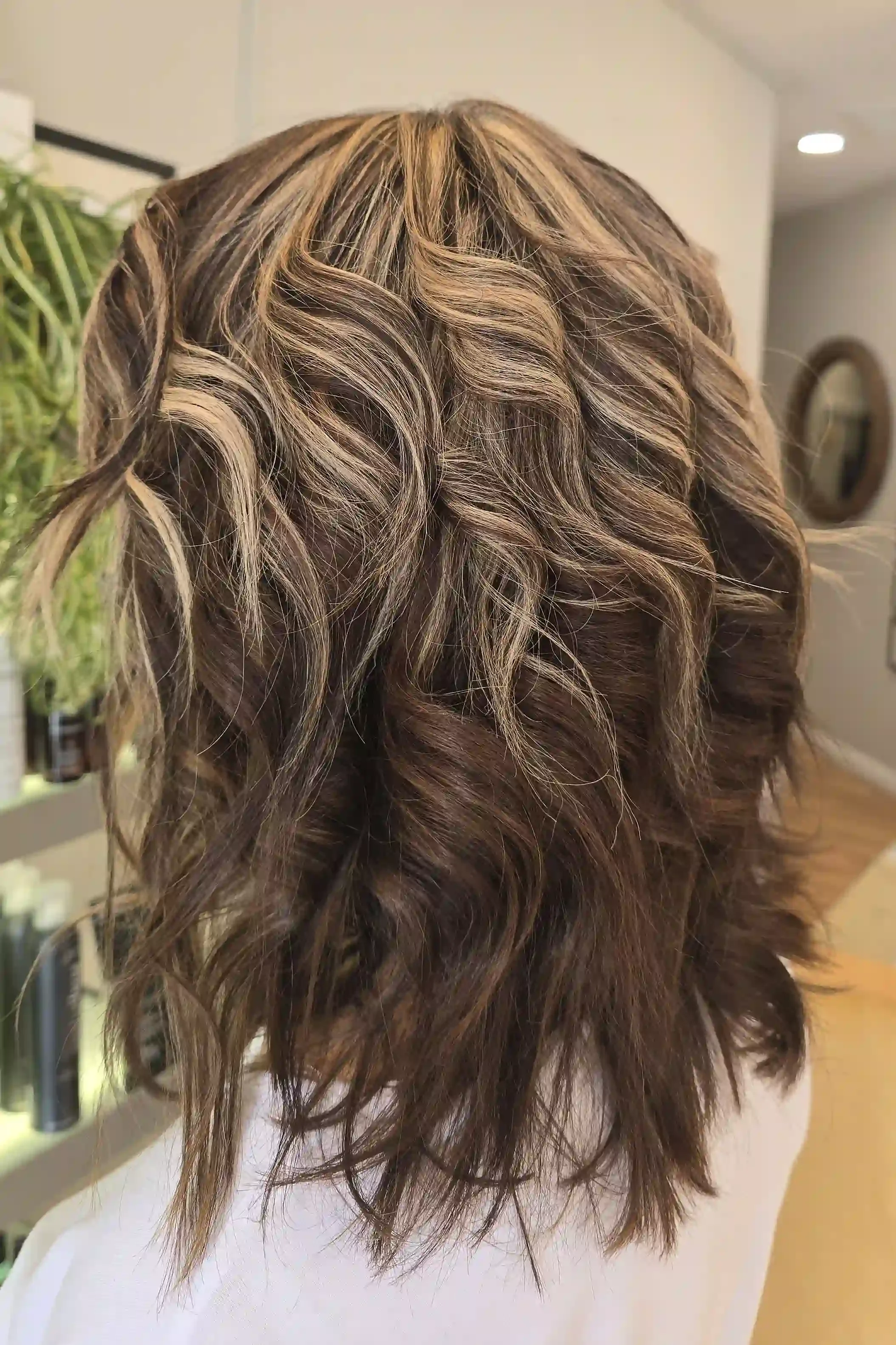 Dimensional brunette wavy lob with soft blonde highlights and loose textured waves, created by Jhana at Chroma Salon Edmonds.