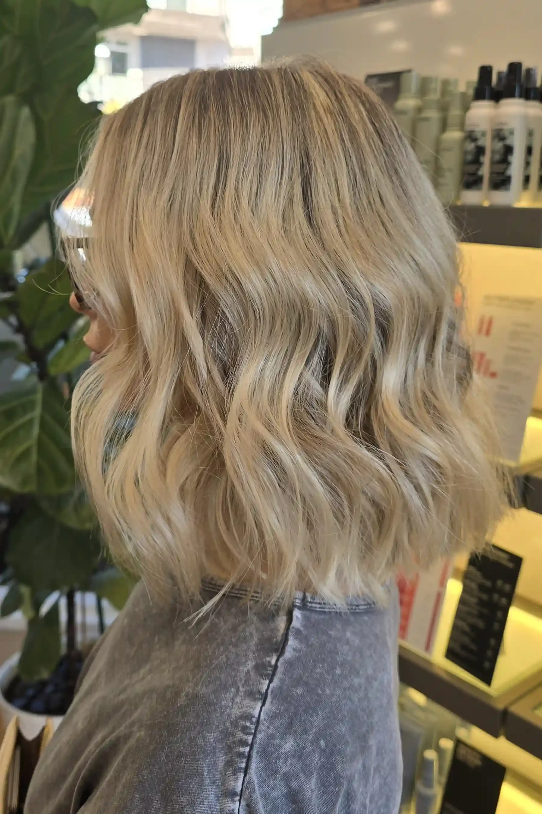 Blonde balayage on a textured long bob featuring soft shadow roots that melt into bright beige blonde ends. Finished with loose beach waves that enhance the dimensional color and create effortless movement. Hair color and styling by Jhana at Chroma S