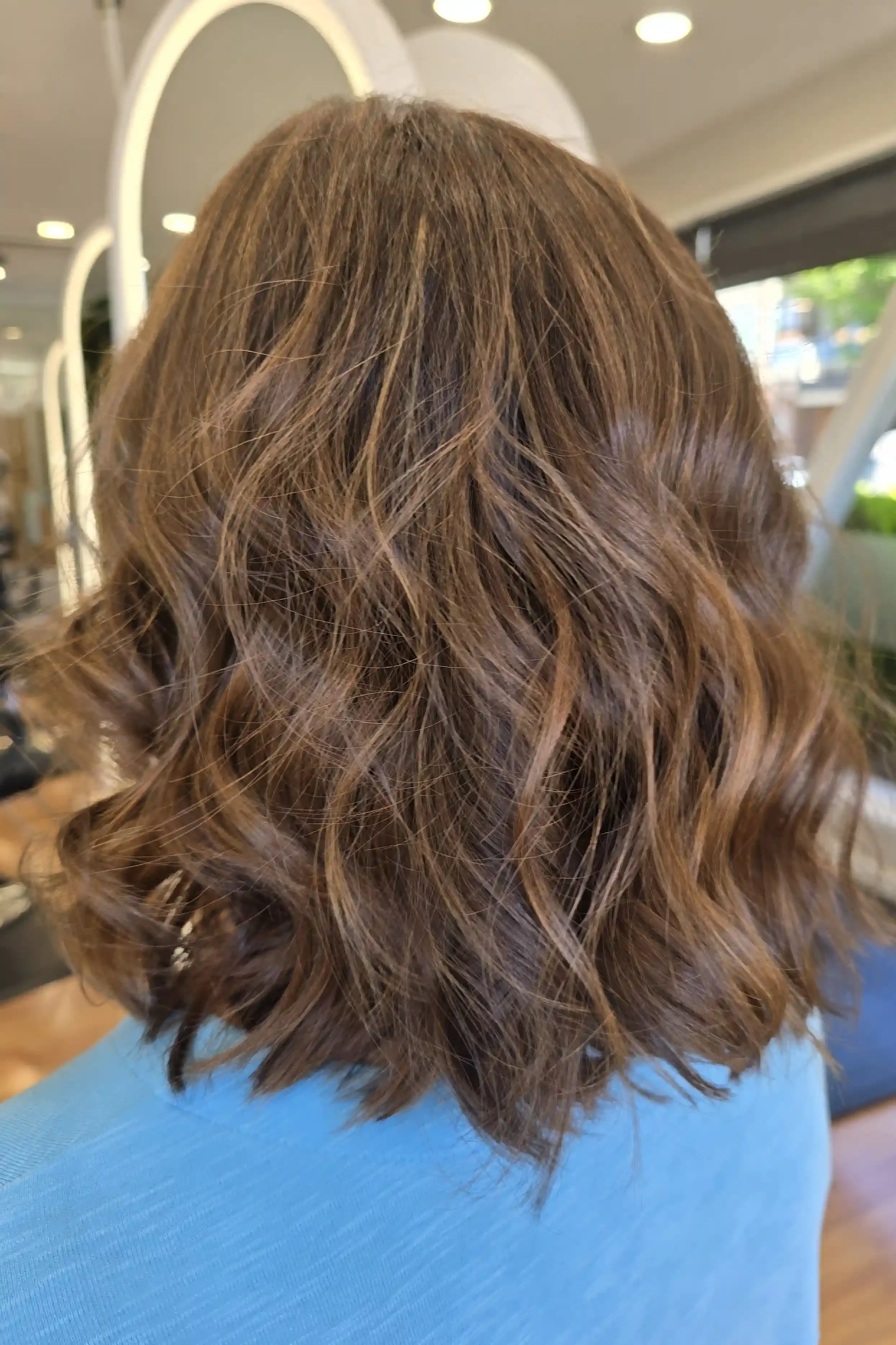 Dimensional brunette balayage on a textured long bob featuring warm mocha and caramel ribbons blended through a rich brown base. Styled with soft, tousled waves to create natural movement and enhance the lived-in color. Hair color and styling by Jhan