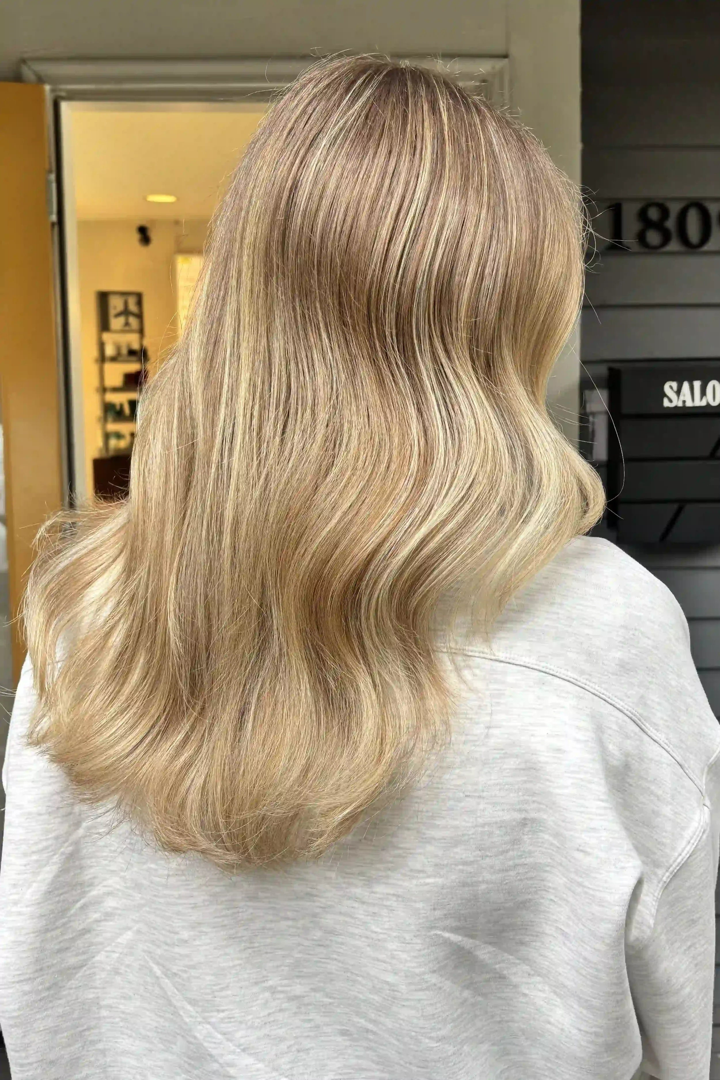 Soft beige blonde hair with finely blended champagne and honey blonde highlights, creating natural-looking dimension and brightness. Long, flowing layers and gentle waves add movement and body, while the smooth, glossy finish enhances the multi-tonal