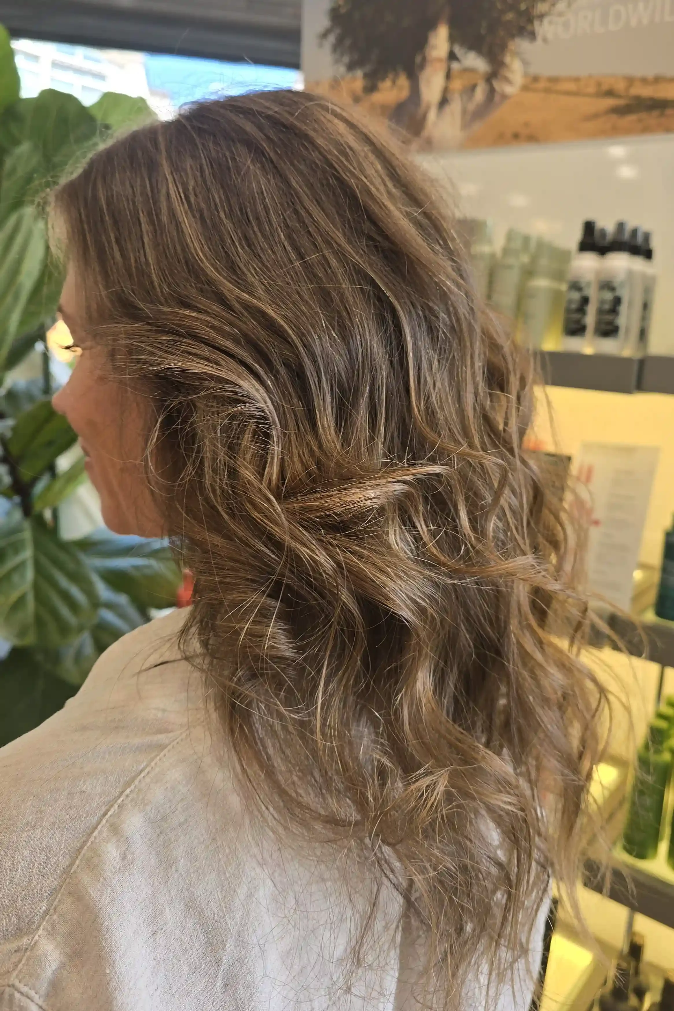 A lived-in brunette balayage with soft caramel dimension, loosely twisted sides, and cascading textured waves. The romantic styling creates effortless volume and movement while showcasing the natural depth and dimension of the color. Hair color and s