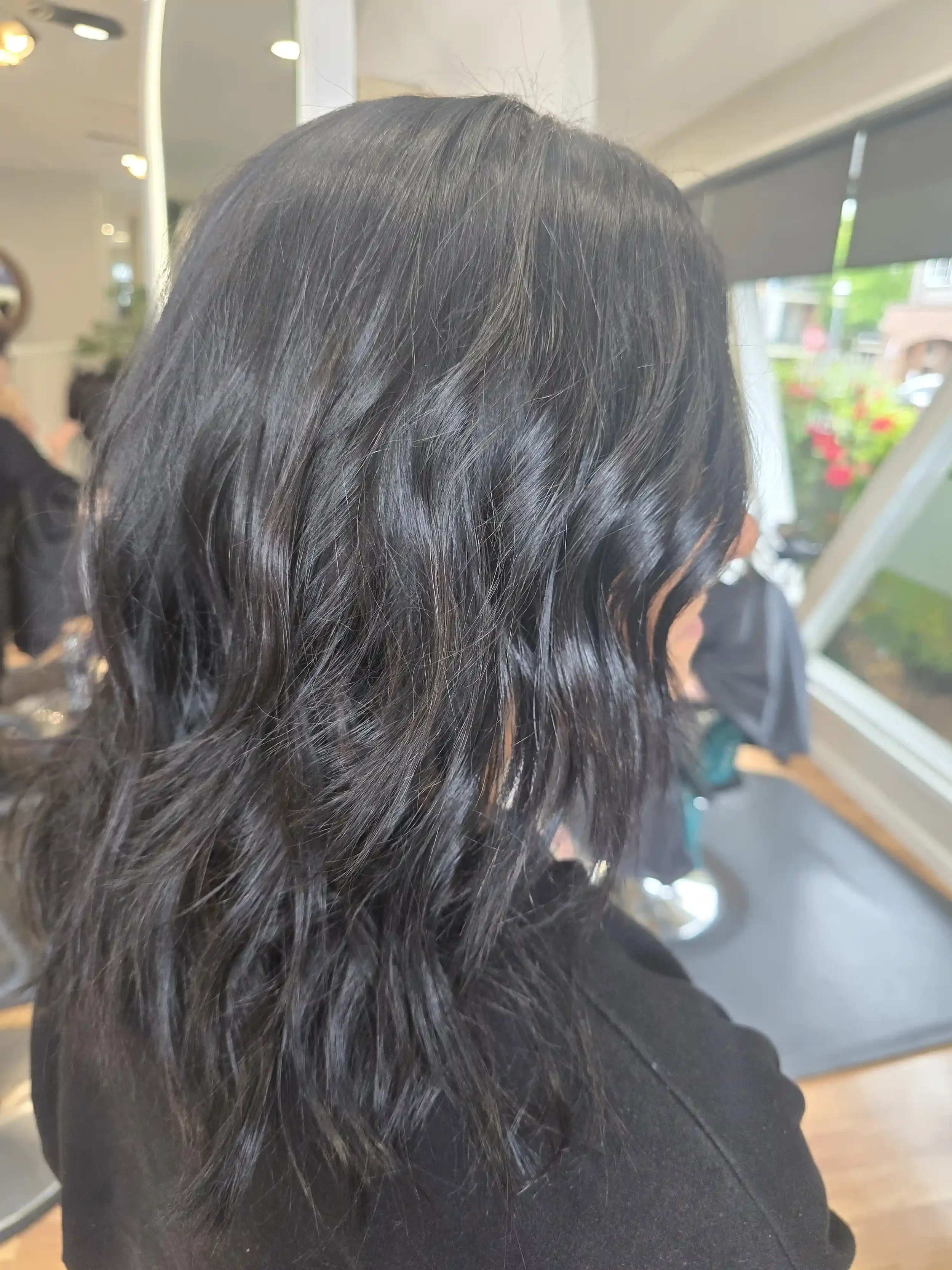 Soft black brunette hair with long layers and loose waves. The rich, dimensional dark color creates a glossy finish while maintaining softness and movement through the mid-lengths and ends. Color and style by Jhana at Chroma Salon Edmonds.