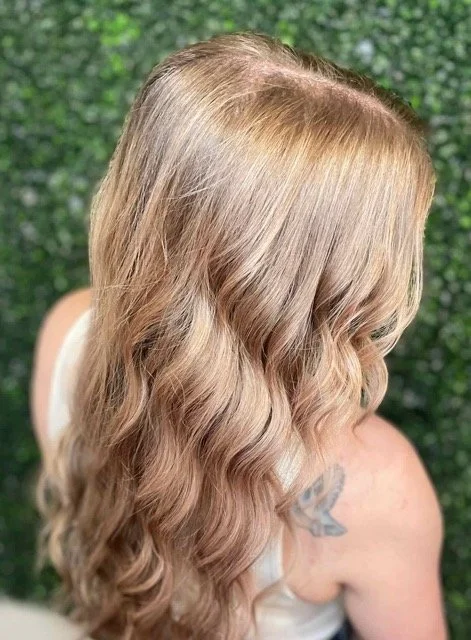 Back view of long, wavy champagne blonde hair with a soft shine and natural volume. Styled by a professional at a Seattle hair salon using Aveda products.