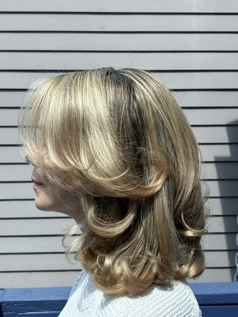 Buttery blonde hair with butterfly layers, voluminous curls, and sweeping curtain bangs, styled by Peter at Chroma Salon Queen Anne Seattle.
