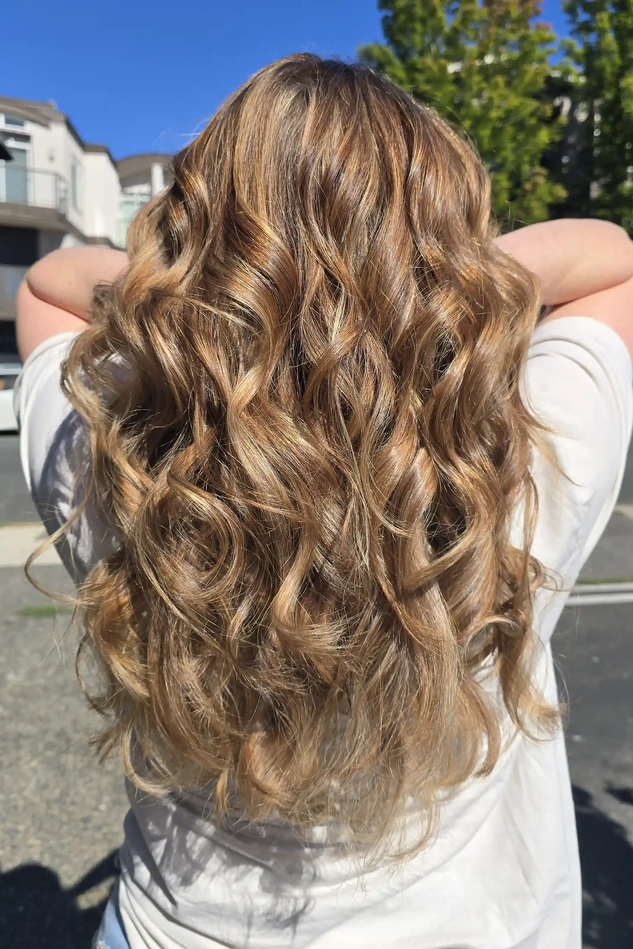 Honey blonde balayage with dimensional caramel lowlights and bright face-framing highlights, styled in long, voluminous curls. The seamless blend creates a soft, sun-kissed finish with exceptional depth, shine, and movement. Hair color and styling by
