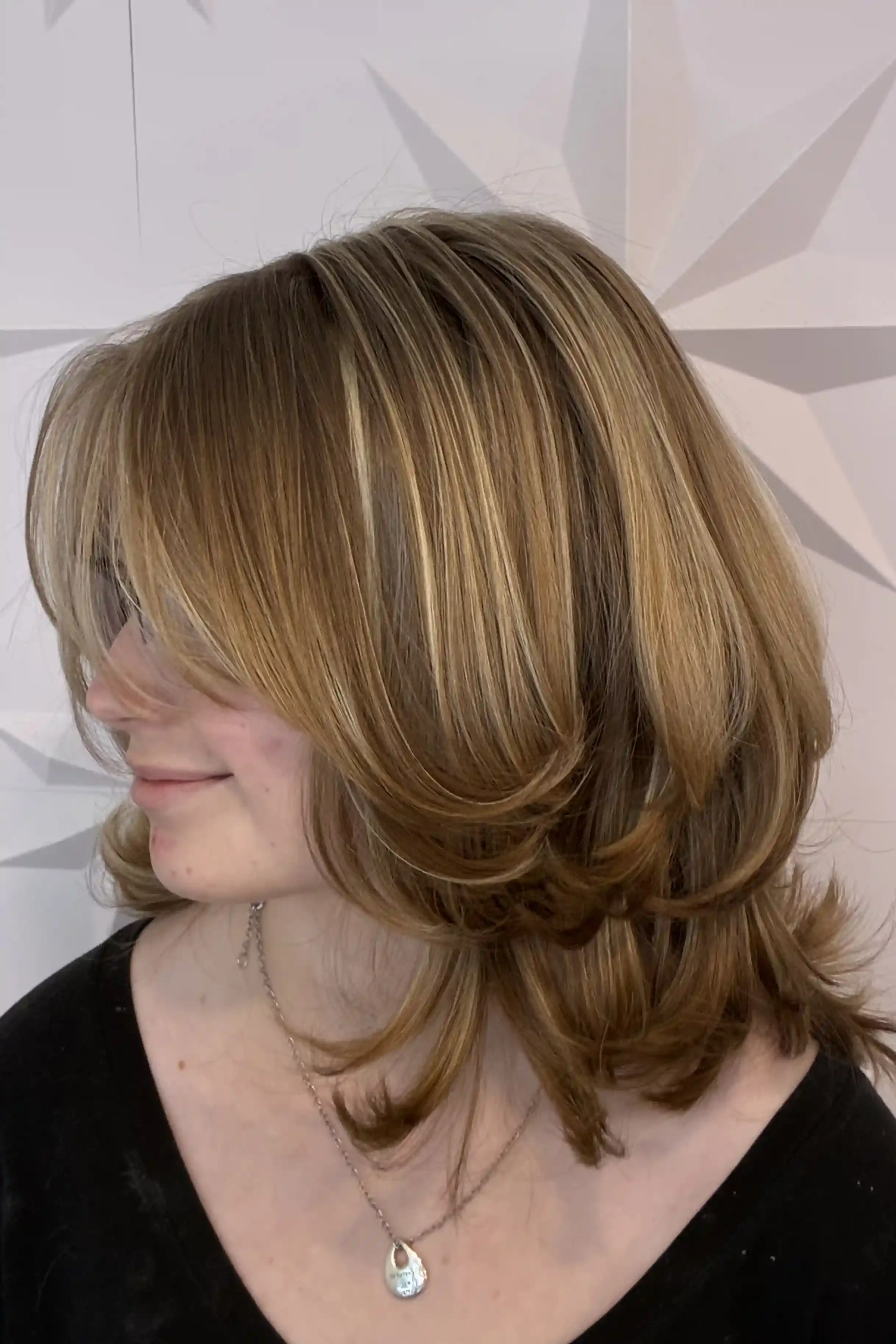 Golden bronde layered bob with soft caramel and blonde dimension, styled with sweeping curtain bangs and rounded, bouncy layers. The polished finish gives the cut movement, fullness, and a soft retro-inspired shape. Hair color, haircut, and styling b