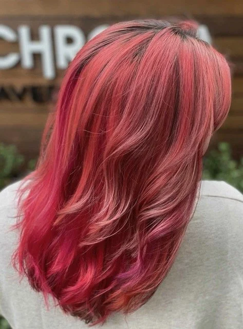 Vibrant pink and magenta dimensional hair color with soft waves, photographed outside Chroma Salon.