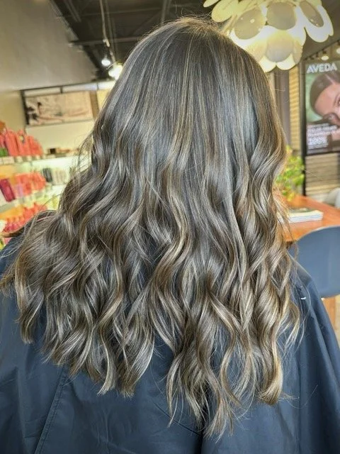 Cool-toned brunette balayage with soft waves and blended highlights, created at Chroma Salon using professional Aveda hair color.