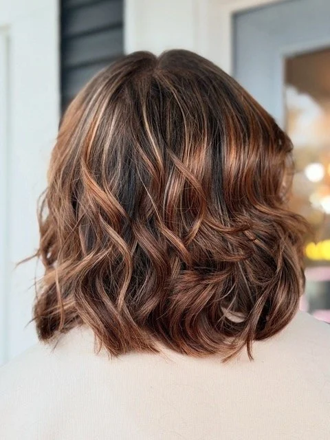 Wavy brunette bob with warm caramel highlights and soft texture, created by Stormi at Chroma Salon Queen Anne Seattle for dimensional movement and shine.
