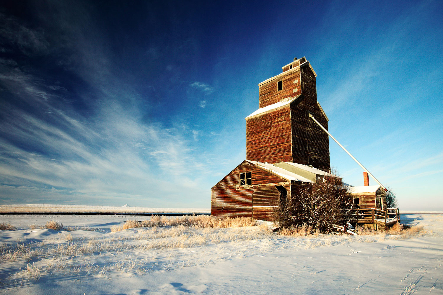 An old, broken down grain elevator sits quietly in the cold western snow.&nbsp;→ Buy a Print