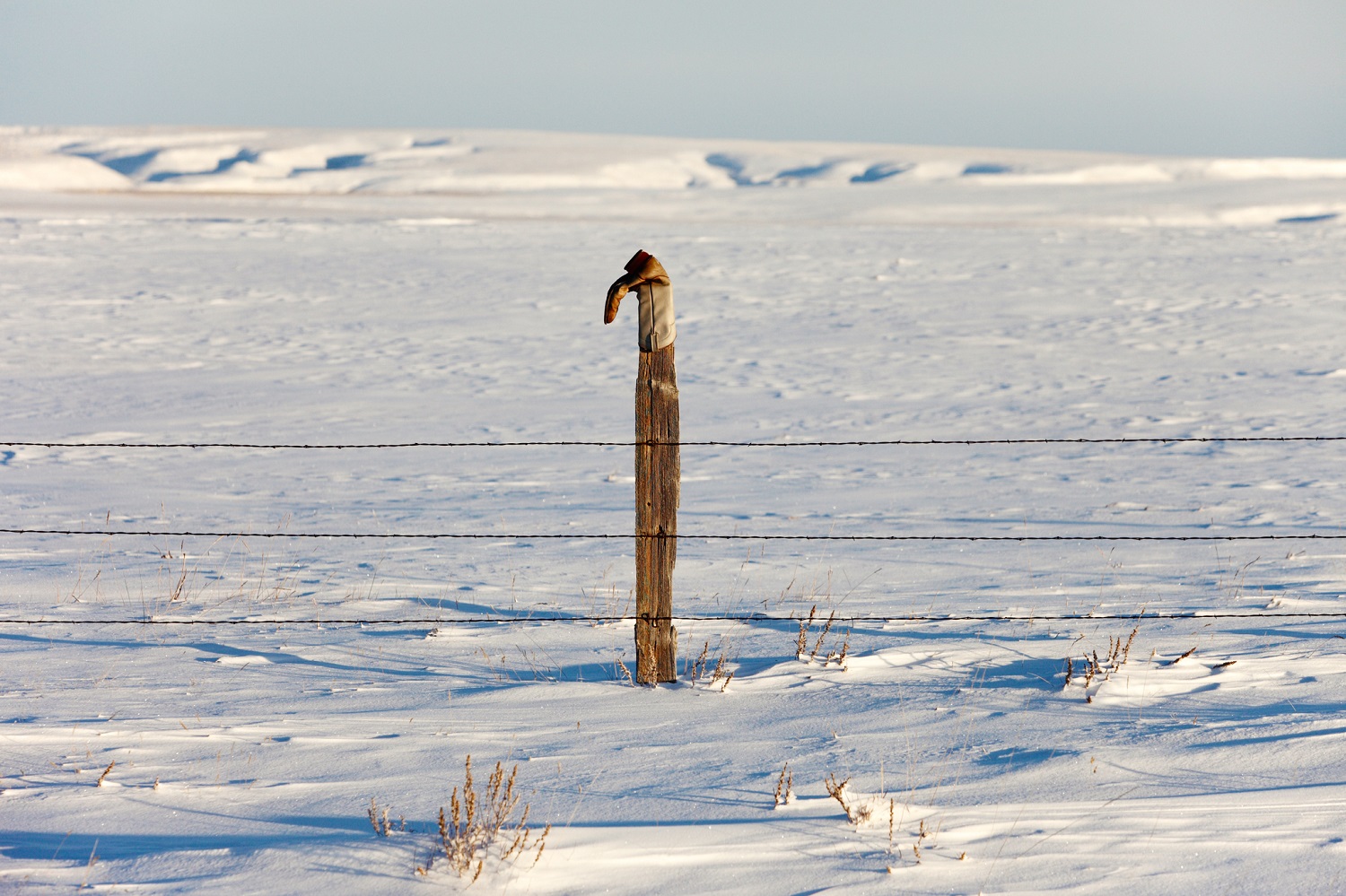 A lonely cowboy boot perched high atop a wooden fence post out in the middle of Montana. → License Photo