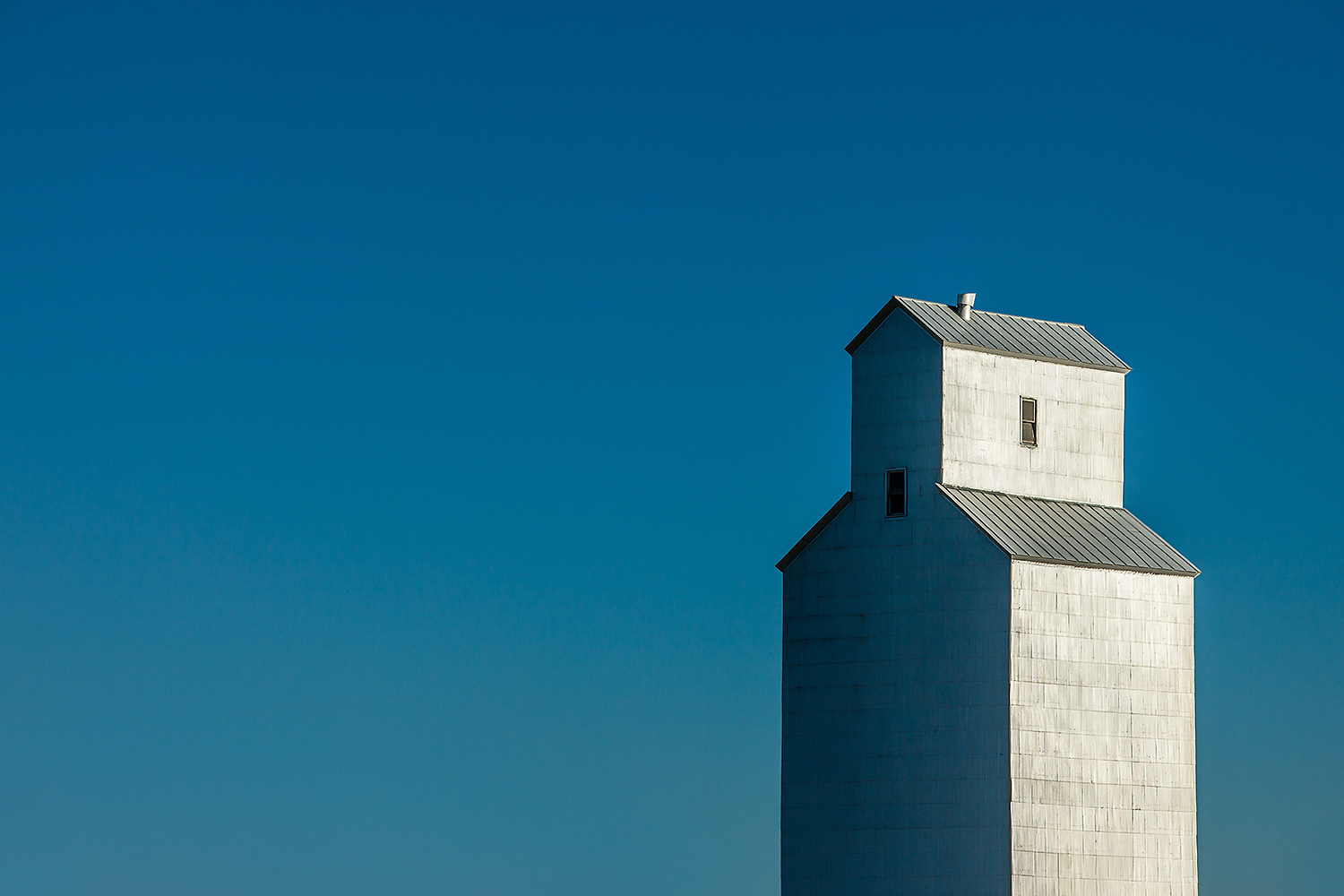 A solitary grain elevator shrouded in sheet metal against a steel blue sky in Gildford, Montana.&nbsp;→ Buy a Print