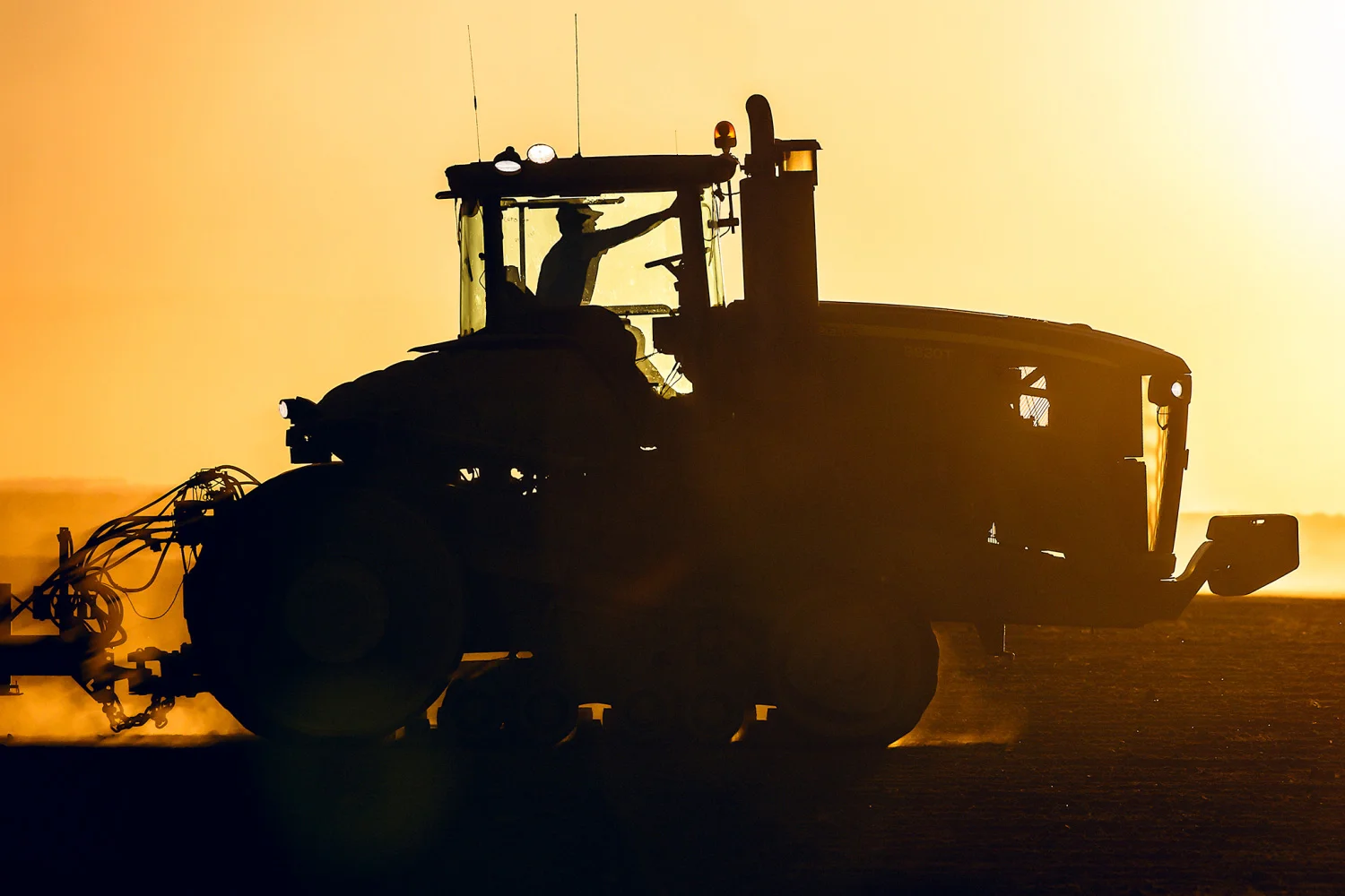 A silhouette of a John Deere tractor seeding wheat on a farm near Chinook, Montana. → License Photo