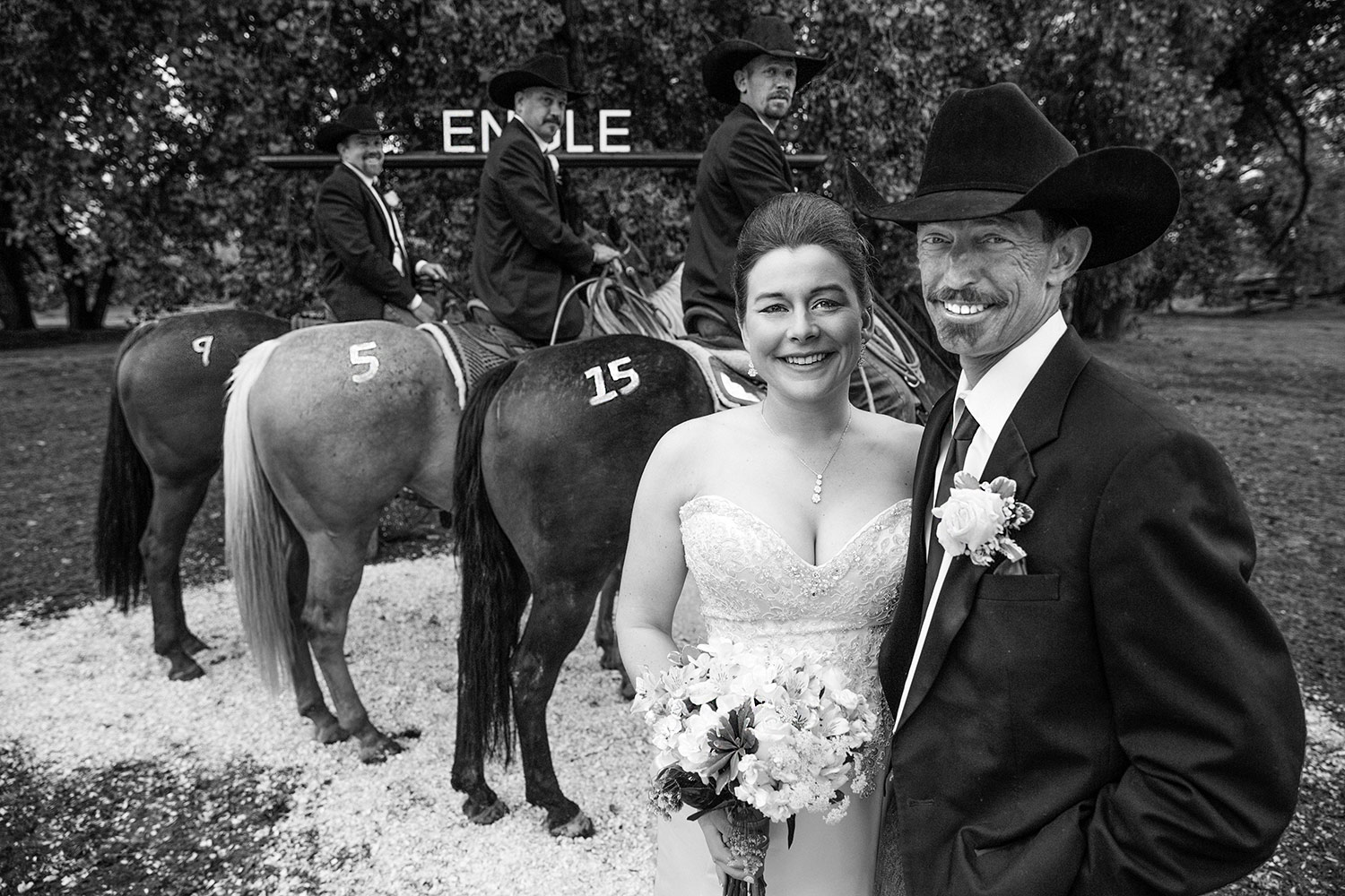 The bride and groom pose for a photograph in front of the groomsmen on horseback, who have the date of the wedding 'branded' on their horses near Chinook, Montana.