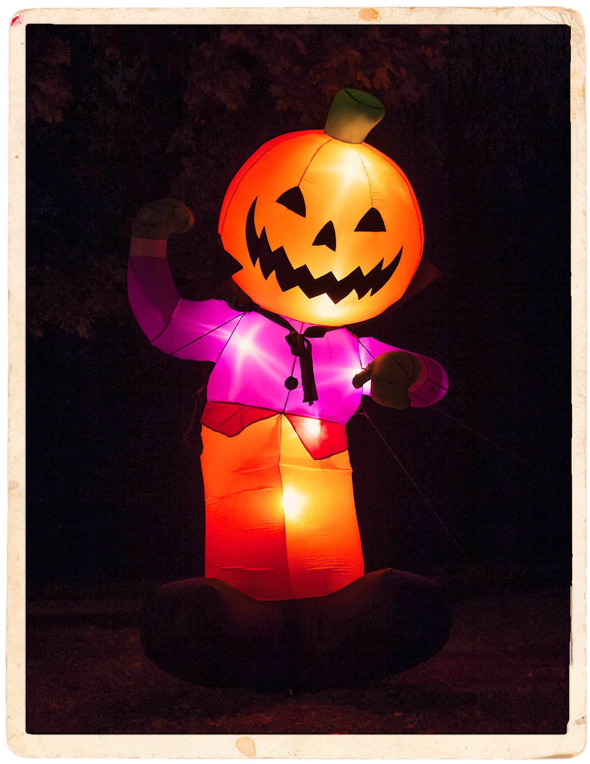 An inflatable jack-o'-lantern man and Halloween display in a yard photographed at night.