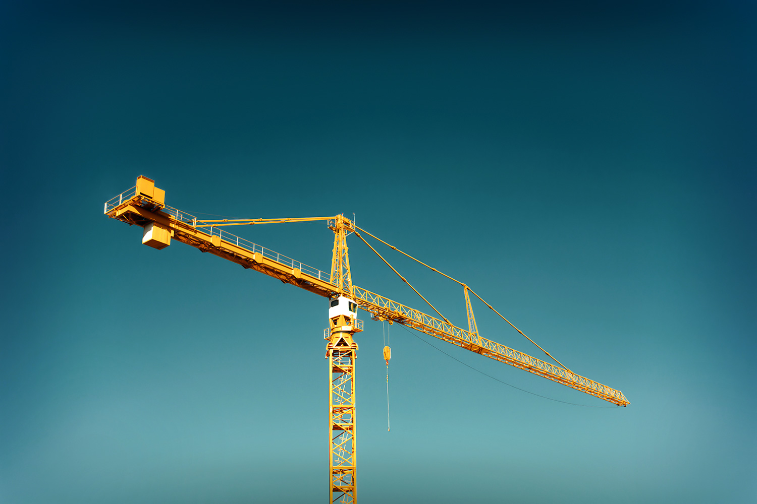 A bright yellow hammerhead tower crane stands alone against a perfectly clear blue sky.&nbsp;→ License Photo