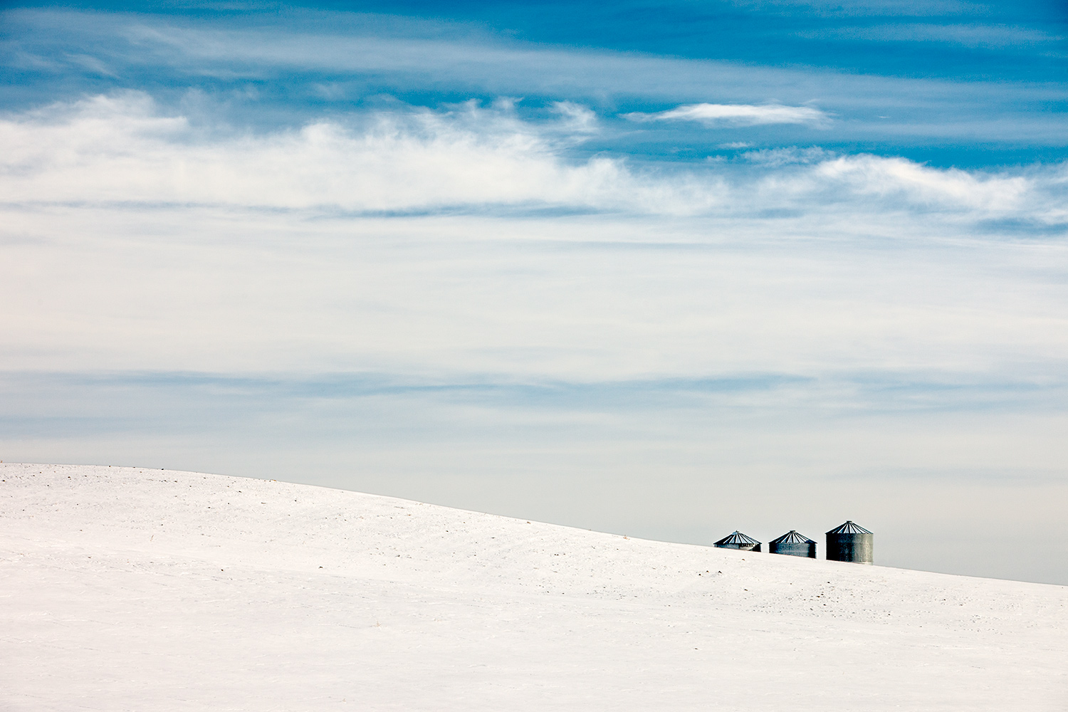 A trio of grain bins lurk over the horizon on what is an otherwise bleak, snowy landscape near Big Sandy, Montana.&nbsp;→ Buy a Print&nbsp;or License Photo