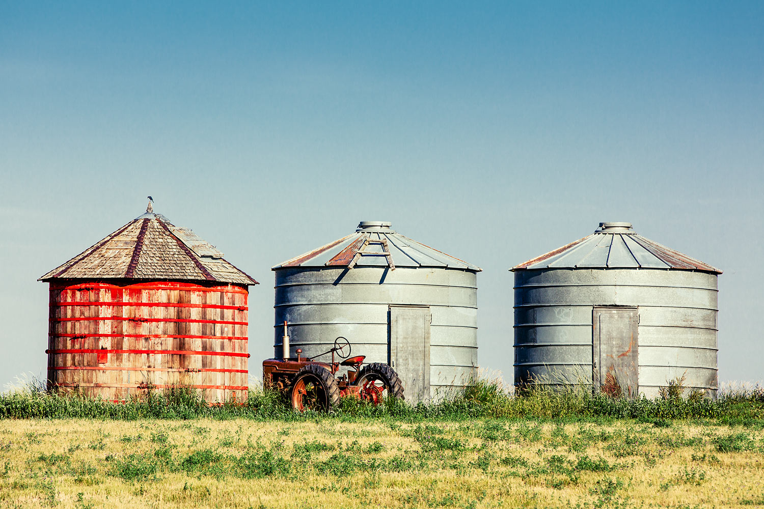 Three bins and an old antique tractor sit in the middle of a field near Lewistown, Montana.&nbsp;→ Buy a Print&nbsp;or License Photo