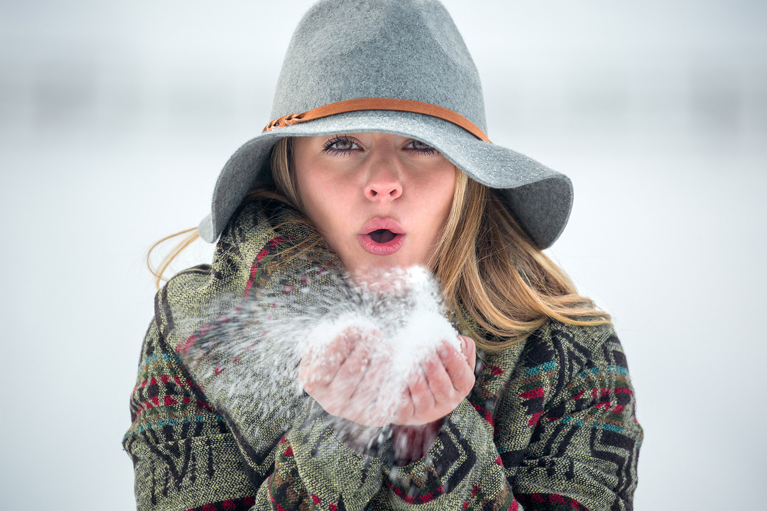 A cowgirl photo of a young woman blowing snow from her hands on a cold winter day outside of Four Corners, Montana.
