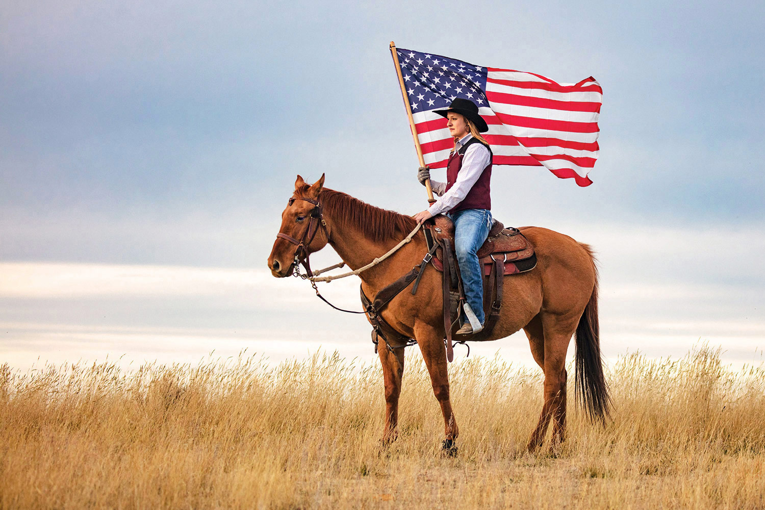 A cowgirl riding horseback with an American flag near Box Elder, Montana. To see more cowgirl photos click here: Cowgirl Photos