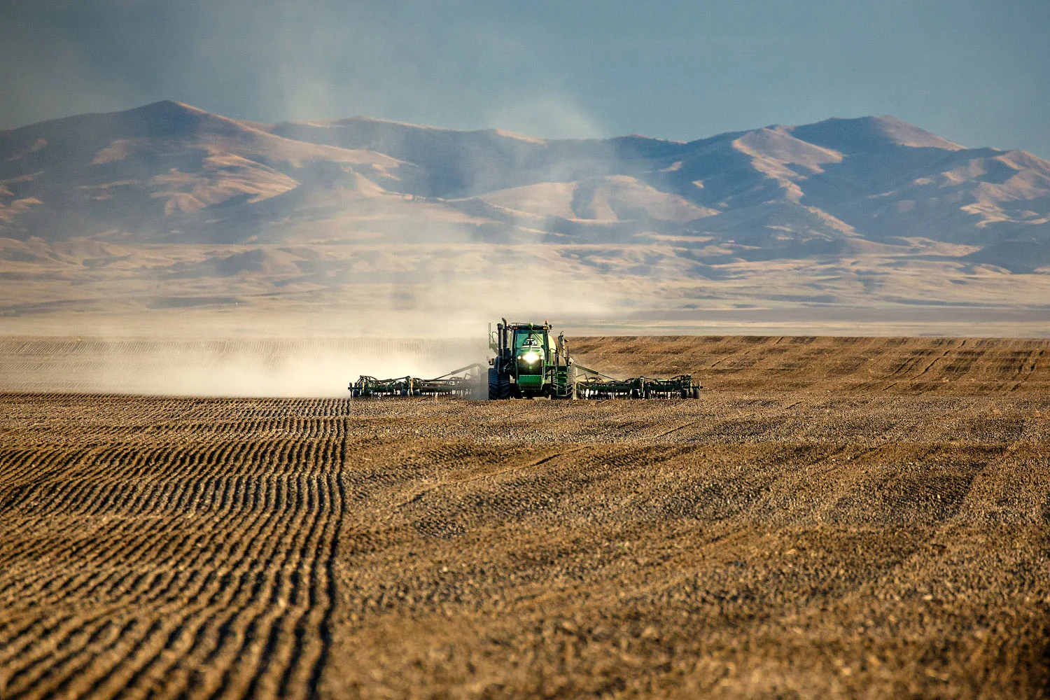 A tractor seeds wheat with mountains in the background near Chinook, Montana. → Buy a Print or License Photo